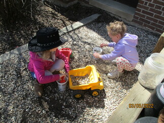 Picture of two prekindergarten children play outside with a toy truck and gravel