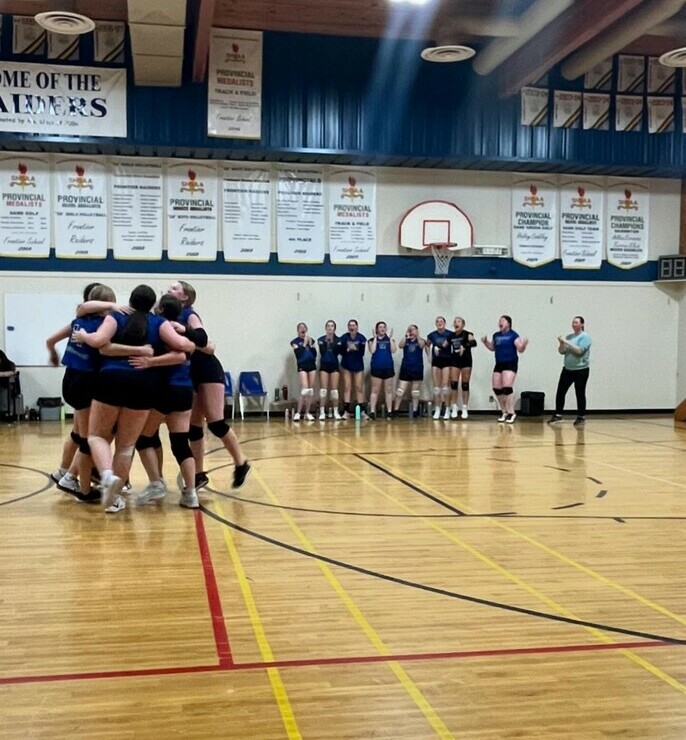 Female volleyball players celebrating on the court with a group hug